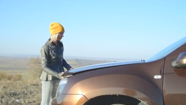 Блондинка в крышке выглядит открытой капот автомобиля ищет недостатки, но не знает точно, где искать — стоковое видео