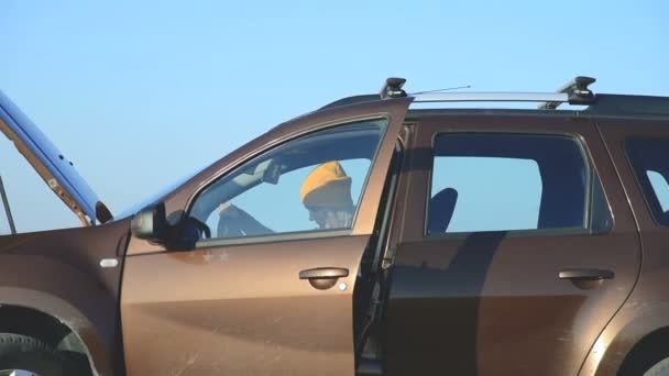 Una chica rubia que encuentra una falla en su SUV sale del coche y abre la capucha. Vista exterior — Vídeo de stock