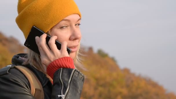 Макро приваблива дівчина кавказьких в жовті капелюхи що говорить на її мобільний телефон на свіжому повітрі восени. Посміхається дівчина в спілкуванні — стокове відео