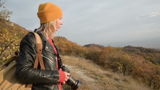 Close-up een aantrekkelijke Kaukasische meisje in een gele hoed neemt af op haar Slr camera buiten in de herfst. Lachende meisje in de werken — Stockvideo