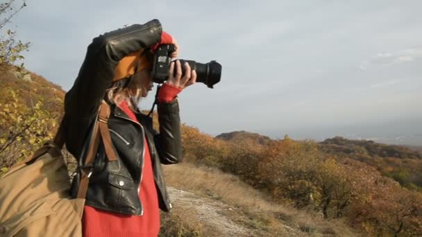 Közeli egy vonzó kaukázusi lány egy sárga kalapban leveszi a tükörreflexes fényképezőgép szabadban ősszel. Mosolygó lány a munkálatok — Stock videók