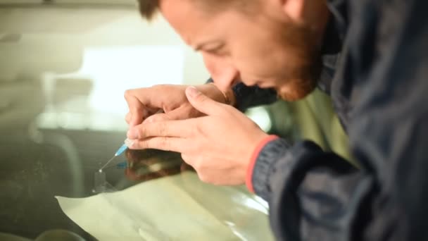 Gros plan d'un homme professionnellement engagé dans l'atelier pour éliminer les fissures sur le pare-brise de la voiture. Remplissage de la fissure avec du polymère 