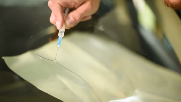 Close-up van een man in de workshop professioneel betrokken bij het uitbannen van scheuren op de voorruit van de auto. De spleet vullen met polymeer — Stockvideo