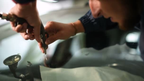 Nahaufnahme eines Mannes, der professionell in der Werkstatt damit beschäftigt ist, Risse an der Windschutzscheibe des Autos zu beseitigen. Lufttrocknung — Stockvideo