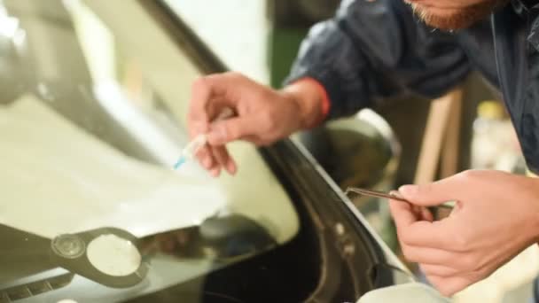 Primo piano di un uomo professionalmente in officina impegnato nell'eliminazione delle crepe sul parabrezza dell'auto. Riempire la fessura con polimero — Video Stock