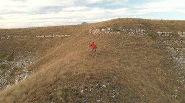 Sakallı hippi erkek bir uzaktan kumandadan bir dron ile hava bir görünümünü günbatımında yayla yakınındaki bir uçurum kenarı boyunca yol gösterir. Adam yar boyunca yürür