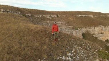 Sakallı hippi erkek bir uzaktan kumandadan bir dron ile hava bir görünümünü günbatımında yayla yakınındaki bir uçurum kenarı boyunca yol gösterir. Cliff üzerinde biri