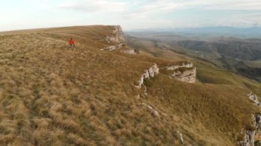 Sakallı hippi erkek bir uzaktan kumandadan bir dron ile hava bir görünümünü günbatımında yayla yakınındaki bir uçurum kenarı boyunca yol gösterir. Adam yar boyunca yürür