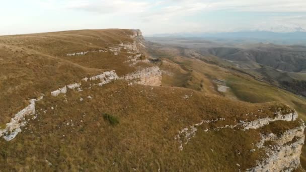 AERIAL: Voo sobre um penhasco alto, revelando uma vista da passagem na Rússia no norte do Cáucaso. Fotografia aérea da estrada no pôr do sol. Voo ao lado da rocha — Vídeo de Stock
