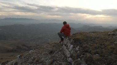 Sakallı hippi erkek bir uzaktan kumandadan bir dron ile hava bir görünümünü günbatımında yayla yakınındaki bir uçurum kenarı boyunca yol gösterir. Adam uçurumun üzerinde oturuyor