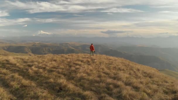 An aerial view of a bearded hipster male with a remote from a drone walks along the edge of a high plateau near a cliff at sunset. The guy walks along the cliff — Stock Video