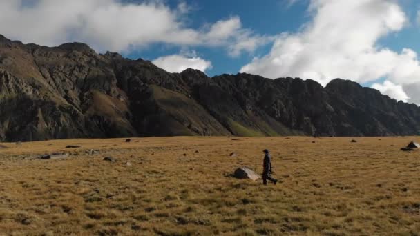 Vista aérea de una fotógrafa caminando sobre una meseta en las montañas con su cámara en el fondo de rocas y montañas. Pasatiempos en la naturaleza 4k — Vídeos de Stock