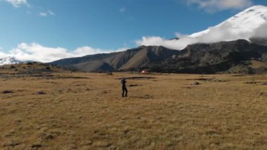 Havadan görünümü ile onun fotoğraf makinesi dağ Elbrus ve kaya arka plan üzerinde dağlarda bir plato üzerinde yürüyen bir kız fotoğrafçı. Şu anki iş doğa 4k