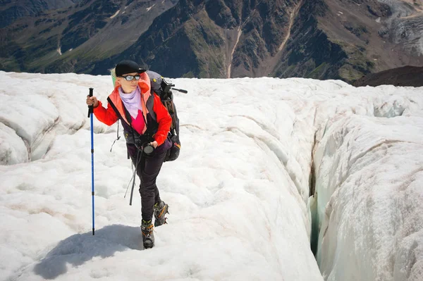 Vrouwelijke bergbeklimmer genieten van de schoonheid van de gletsjer loopt op de gletsjer van de crampon en zonnebril. Tegen de achtergrond van de hoge bergen van de Caucasus lucht en de wolken — Stockfoto