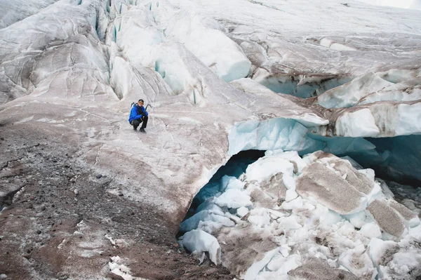 Le voyageur en casquette et lunettes de soleil est assis dans les montagnes enneigées sur le glacier. Voyageur dans un environnement naturel — Photo