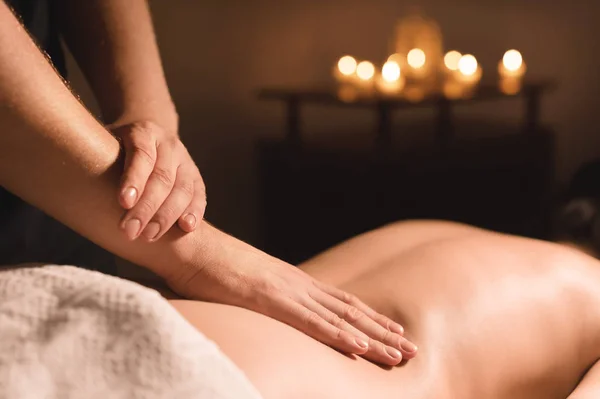 Männerhände in Nahaufnahme, die einem jungen Mädchen in einem dunklen Kosmetikbüro eine heilende Massage mit Öl verabreichen. dunkler Schlüssel — Stockfoto