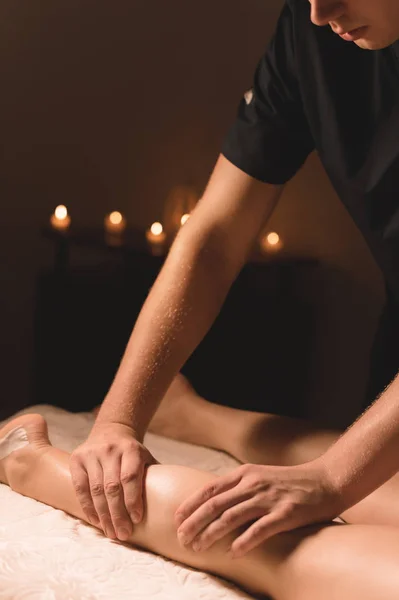 Nahaufnahme männlicher Hände bei der Wadenmassage weiblicher Beine in einem dunklen Raum mit Kerzen im Hintergrund. Kosmetik und Wellnessanwendungen — Stockfoto