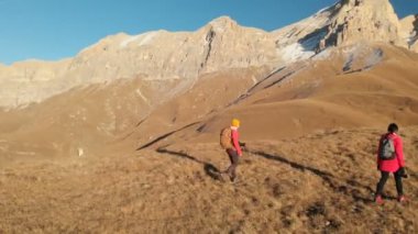 İki kız seyahat sırt çantaları ve kameralar ile havadan görünümü üzerinden tepeler dağlarda epik kayalar arasında yürüyün. Kızlar fotoğrafçılar fotoğraf makinelerine batımında ile