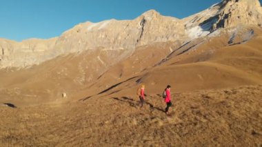 İki kız seyahat sırt çantaları ve kameralar ile havadan görünümü üzerinden tepeler dağlarda epik kayalar arasında yürüyün. Kızlar fotoğrafçılar fotoğraf makinelerine batımında ile