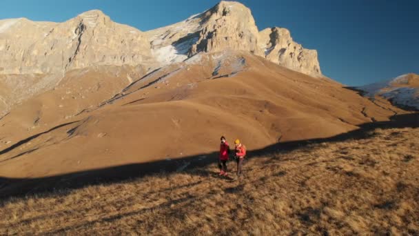 バックパックとカメラと 2 人の女の子の旅行者の空撮は、山々 の壮大な岩の間丘を散策します。夕暮れ時の自分のカメラで女の子の写真家 — ストック動画