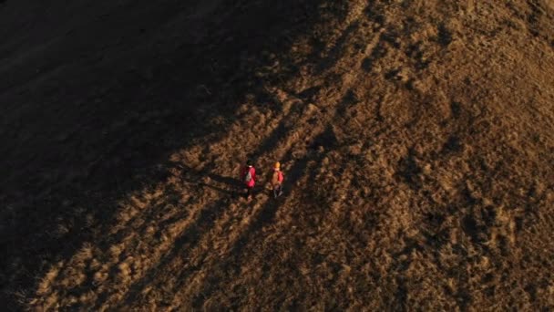 Aerial view of a two girls traveler with backpacks and cameras stroll through the hills between the epic rocks in the mountains. Girls photographers with their cameras at sunset — Stock Video