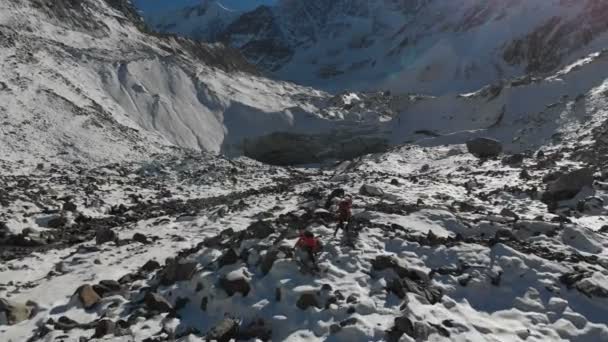 Flygfoto över två flickor resenären med ryggsäckar och kameror gå igenom snön och stenar till glaciären mellan episka stenarna i bergen. Flickor fotografer med sina kameror vid solnedgången — Stockvideo