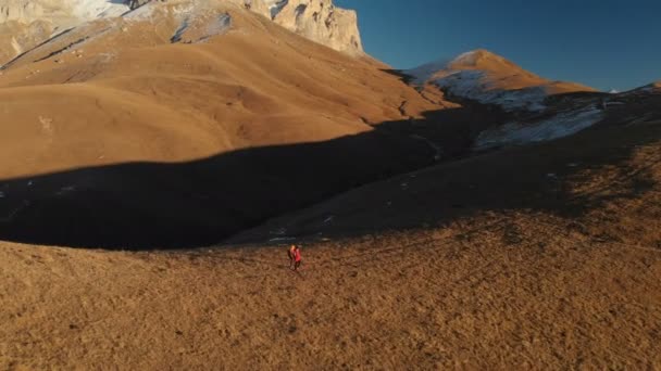 Vista aérea de un viajero de dos chicas con mochilas y cámaras paseando por las colinas entre las rocas épicas de las montañas. Chicas fotógrafas con sus cámaras al atardecer — Vídeos de Stock