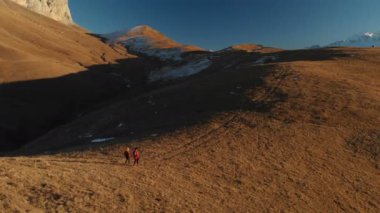 İki kız seyahat sırt çantaları ve kameralar ile havadan görünümü üzerinden tepeler dağlarda epik kayalar arasında yürüyün. Kızlar fotoğrafçılar fotoğraf makinelerine batımında ile