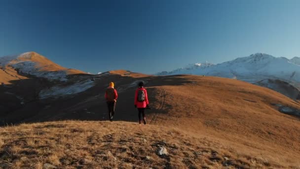 Vista aérea de un viajero de dos chicas con mochilas y cámaras paseando por las colinas entre las rocas épicas de las montañas. Chicas fotógrafas con sus cámaras al atardecer — Vídeos de Stock