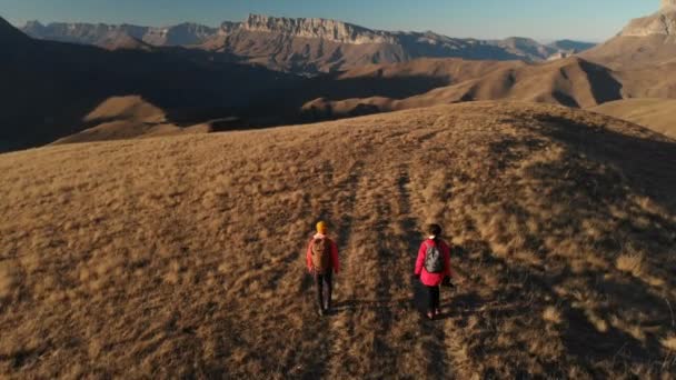 Vista aérea de un viajero de dos chicas con mochilas y cámaras paseando por las colinas entre las rocas épicas de las montañas. Chicas fotógrafas con sus cámaras al atardecer — Vídeos de Stock