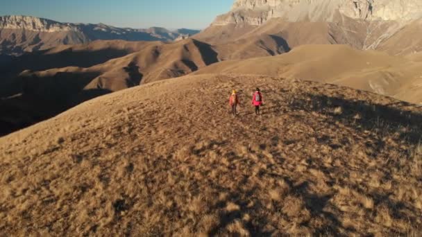 Luchtfoto van een reiziger van de twee meisjes met rugzakken en camera's wandeling door de heuvels tussen de epische rotsen in de bergen. Meisjes fotografen met hun camera's bij zonsondergang — Stockvideo