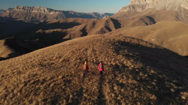 Pemandangan udara dari dua gadis wisatawan dengan ransel dan kamera berjalan-jalan melalui bukit-bukit antara batu epik di pegunungan. Gadis fotografer dengan kamera mereka saat matahari terbenam — Stok Video