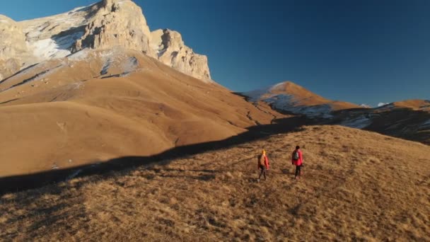 Luchtfoto van een reiziger van de twee meisjes met rugzakken en camera's wandeling door de heuvels tussen de epische rotsen in de bergen. Meisjes fotografen met hun camera's bij zonsondergang — Stockvideo