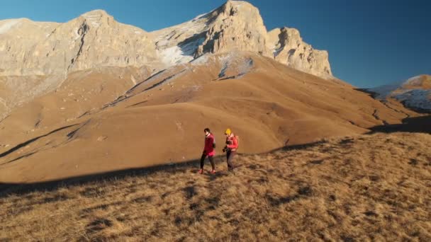 Vista aérea de un viajero de dos chicas con mochilas y cámaras paseando por las colinas entre las rocas épicas de las montañas. Chicas fotógrafas con sus cámaras al atardecer — Vídeo de stock