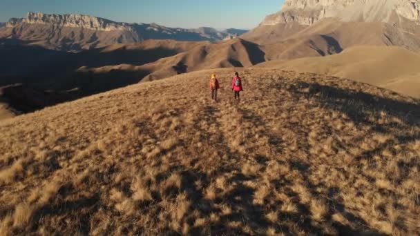 Vista aérea de un viajero de dos chicas con mochilas y cámaras paseando por las colinas entre las rocas épicas de las montañas. Chicas fotógrafas con sus cámaras al atardecer — Vídeo de stock