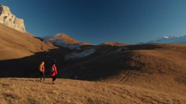 İki kız seyahat sırt çantaları ve kameralar ile havadan görünümü üzerinden tepeler dağlarda epik kayalar arasında yürüyün. Kızlar fotoğrafçılar fotoğraf makinelerine batımında ile