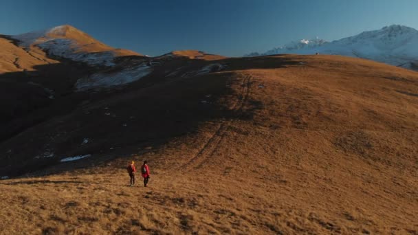 İki kız seyahat sırt çantaları ve kameralar ile havadan görünümü üzerinden tepeler dağlarda epik kayalar arasında yürüyün. Kızlar fotoğrafçılar fotoğraf makinelerine batımında ile — Stok video