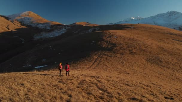 Εναέρια άποψη του ταξιδιώτη δύο κορίτσια με Σακίδια και κάμερες βόλτα στους λόφους ανάμεσα στα επική βράχια στα βουνά. Κορίτσια φωτογράφους με τις φωτογραφικές μηχανές τους στο ηλιοβασίλεμα — Αρχείο Βίντεο