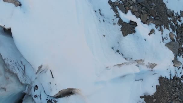 Vista aérea close-up borda de uma geleira fluindo coberto com neve e pedras altas nas montanhas. Destruição natural dos glaciares de fusão e aquecimento global — Vídeo de Stock