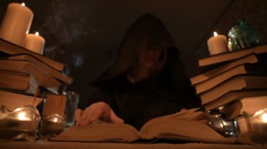Mum ışığı ve seyir için bir kitap üzerinde bir büyü tarafından karanlık bir odada bir başlıklı orta yakın çekim kız sihirbaz. Düşük anahtar. Mistik küçük Dof