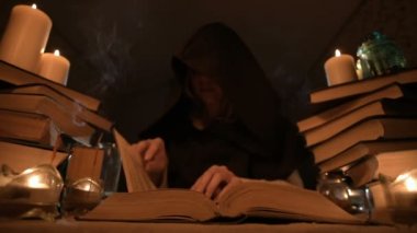 Mum ışığı ve seyir için bir kitap üzerinde bir büyü tarafından karanlık bir odada bir başlıklı orta yakın çekim kız sihirbaz. Düşük anahtar. Mistik küçük Dof