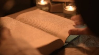 Bir büyük yakın çekim kız sihirbaz bir büyü bir kitap arıyorum mum ışığı ile karanlık bir odada. Düşük anahtar canlı kamera. Mistik. Küçük Dof