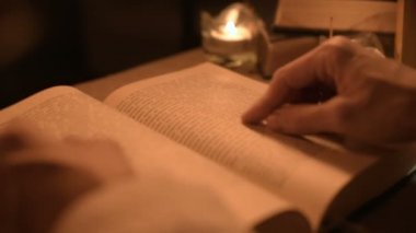Bir büyük yakın çekim kız sihirbaz bir büyü bir kitap arıyorum mum ışığı ile karanlık bir odada. Düşük anahtar canlı kamera. Mistik. Küçük Dof