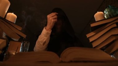Mum ışığı içinde karanlık bir odada bir sıkılmış kız sihirbaz Close-up bir kitapta dabbles ve derin derin düşünür. Düşük anahtar canlı kamera. Mistik. Küçük Dof