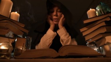 Mum ışığı içinde karanlık bir odada bir sıkılmış kız sihirbaz Close-up bir kitapta dabbles ve derin derin düşünür. Düşük anahtar canlı kamera. Mistik. Küçük Dof