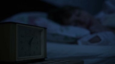 Bir kız yatakta yatarken pijama yakın çekim ve bir alarm saat bakarak uyumak yapamaz. Yüz kızlar için değişken odak saatten. Amerikan gece etkisi. Düşük anahtar soğuk ışık İmitasyon gece