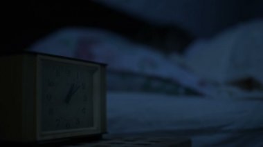 Bir kız yatakta yatarken pijama yakın çekim ve bir alarm saat bakarak uyumak yapamaz. Yüz kızlar için değişken odak saatten. Amerikan gece etkisi. Düşük anahtar soğuk ışık İmitasyon gece