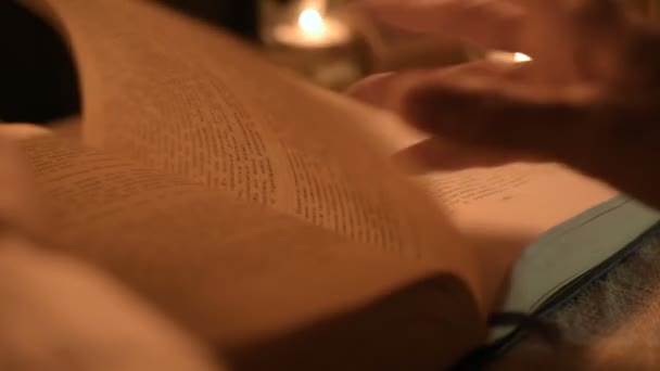 Big Close-up girl magician in a dark room with candlelight looking for a spell in a book. Low key live camera. Mystic. Small DOF — Stock Video