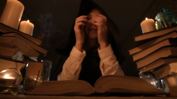 Gros plan d'une magicienne qui s'ennuie dans une pièce sombre à la lueur des chandelles tremble dans un livre et médite. Caméra basse en direct. Mystique. Petit DOF — Video