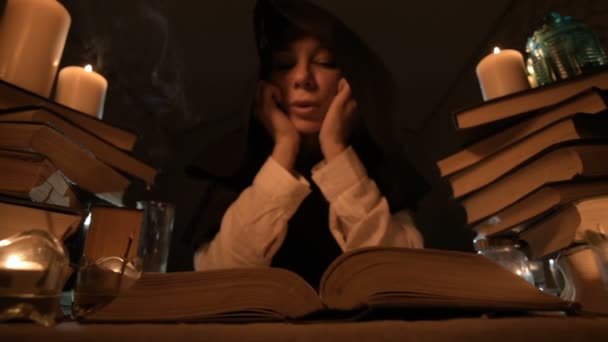 Крупный план скучающей девушки-фокусницы в темной комнате при свечах балуется в книге и медитирует. Низкокачественная камера. Мистик. Небольшой DOF — стоковое видео